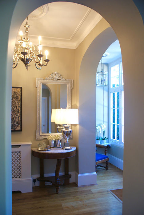 Large airy Edwardian hall with khaki painted walls, traditional plasterwork and features, wooden floor. The feature furniture is a marble top entrance console table, with large table lamp.