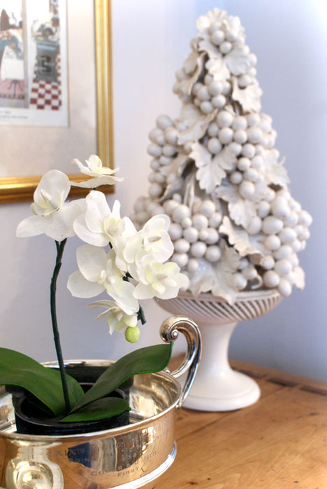 White porcelain fruit topiary ornament, orchid plant in a silver pot, artwork print behand.
