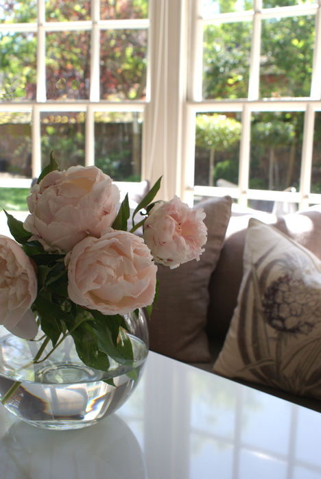 White Carrara marble topped island reflects the light back into the room, peonies in a globe vase with floral throw cushions.