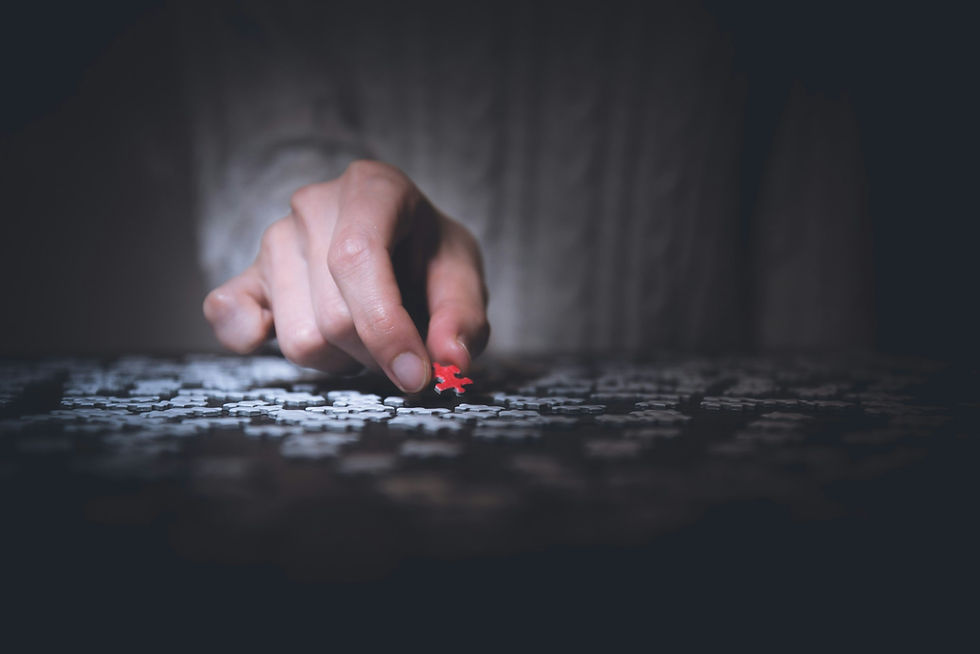 man's hand placing red puzzle piece among white puzzle pieces