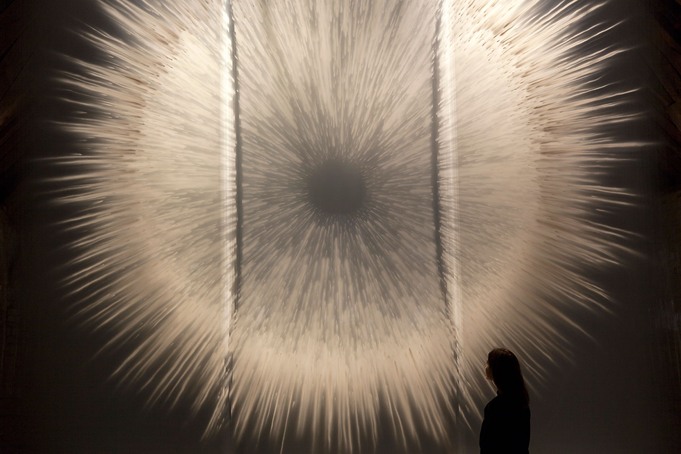 A person observes a large, radial light art installation with streaks emanating from a central dark point, creating a dramatic visual effect.
