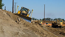 Dozer grading a levee slope on a civil construction site with earthmoving equipment working in the background.