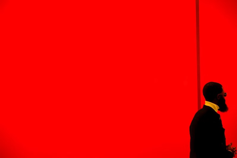 Man in a suit and sunglasses stands against a vibrant red background, creating a bold contrast.