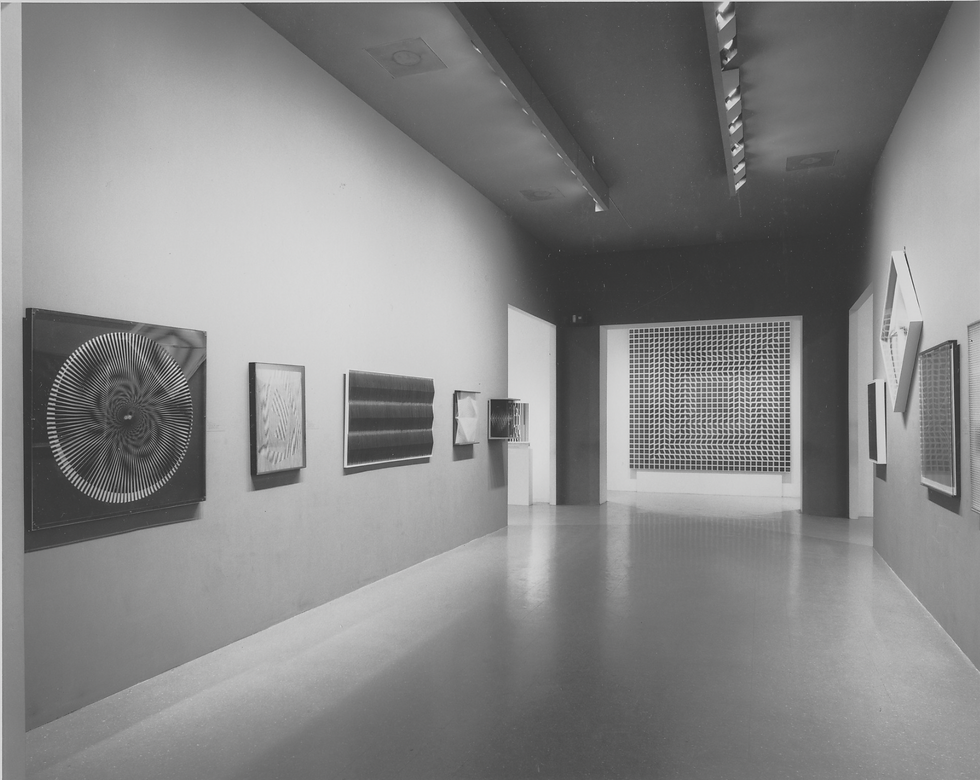 Art gallery hallway displaying abstract black and white geometric artworks on walls. Fluorescent lighting casts soft shadows, creating a modern, serene ambiance.