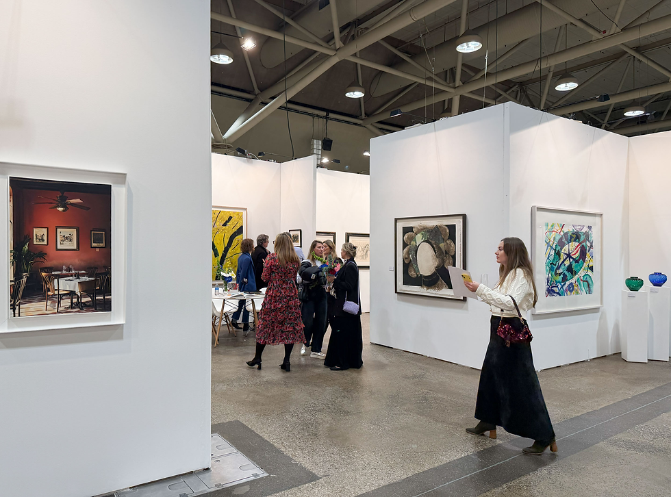 Art gallery scene with people viewing colorful paintings. A woman in a white sweater holds a paper. White walls and framed art surround them.