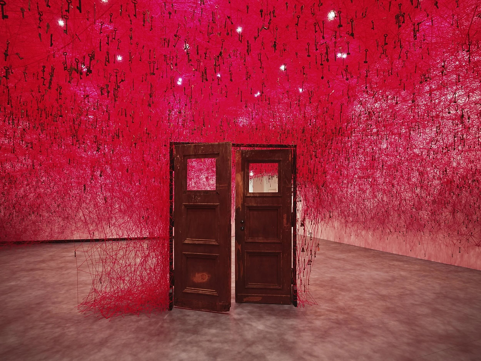 Art installation with two wooden doors amid a red web of strings and hanging keys in a gallery.