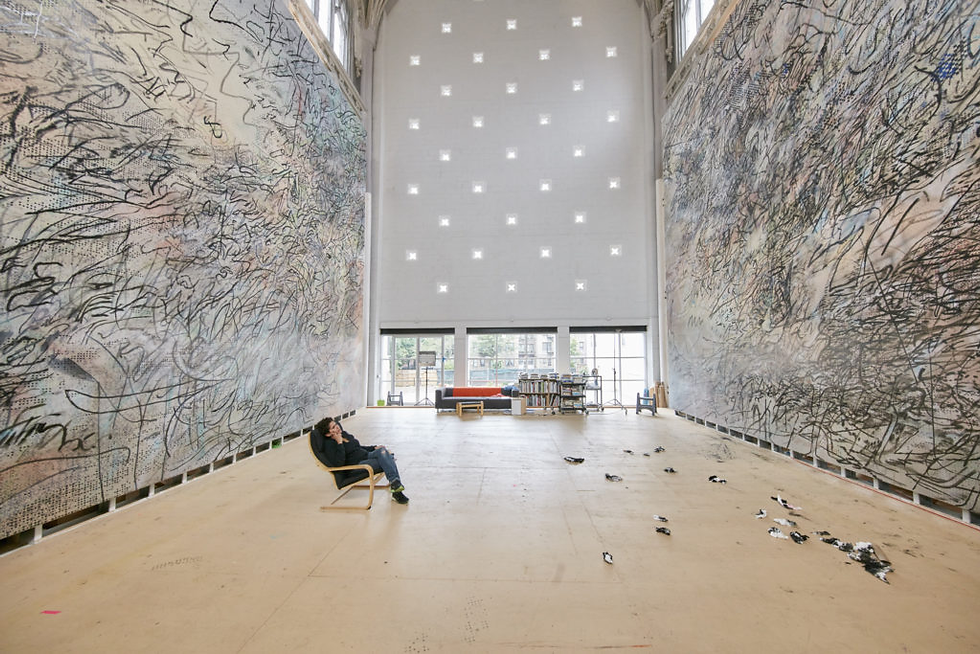 Expansive room with abstract murals on walls. Person in chair gazes at them. Sunlight filters in through windows. Calm, contemplative mood.