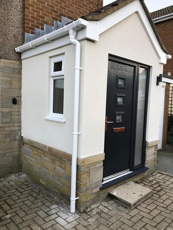 Newly upgraded porch with a modern black door with a frosted side panel to the right to give additional light. There is also a window to the side. The finish is stone and a light cream render.