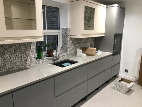 An image of a newly installed kitchen mixing both grey and white cupboards and patterned white and grey tiles to constrast. 