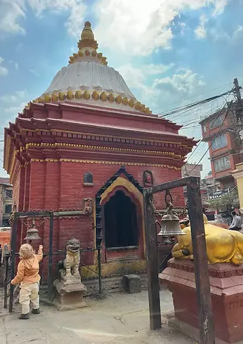 Bambino che suona una campana davanti a un piccolo tempio lungo la strada, momento di scoperta durante un viaggio in famiglia in Nepal.