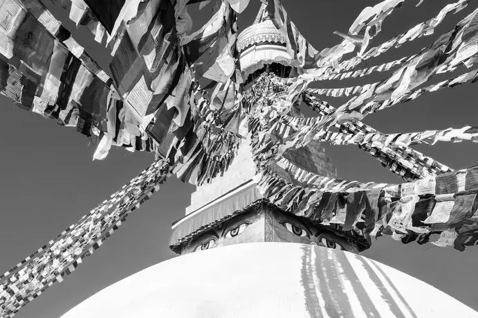 Dettaglio degli occhi di Buddha sulla stupa di Boudhanath a Kathmandu, tra file di bandierine colorate mosse dal vento.