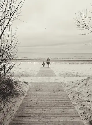 Mamma e figlio che camminano lungo una spiaggia del Mar Baltico, costa invernale, sabbia chiara e mare aperto sullo sfondo.