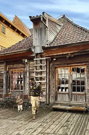 Papà e figlio che camminano tra i vicoli colorati di Bryggen, tra case di legno e storia norvegese, in un viaggio di scoperta familiare.