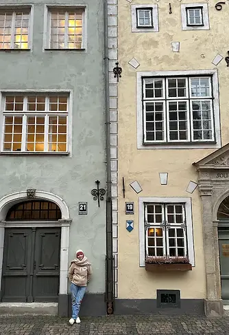 Mamma in piedi tra le case medievali dei Tre Fratelli a Riga, stretto passaggio architettonico con facciate storiche