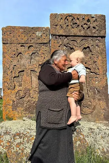 Bambino in braccio a una donna armena davanti alle tradizionali croci di pietra (khachkar), durante un incontro di condivisione in Armenia.
