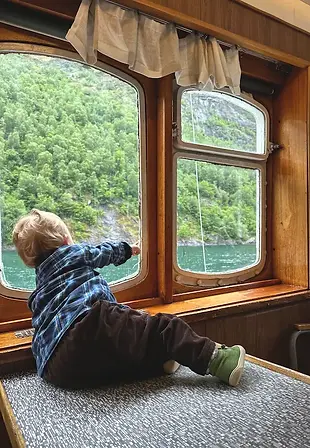 Bambino meravigliato che guarda dalla finestra durante la navigazione nel fiordo di Geiranger, tra luce, acqua e silenzi