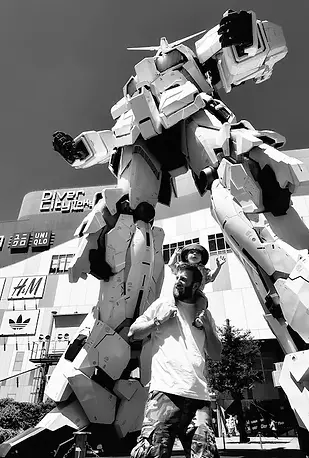 Papà e figlio in posa davanti alla statua gigante del Gundam a Tokyo, il robot luminoso che domina la piazza.
