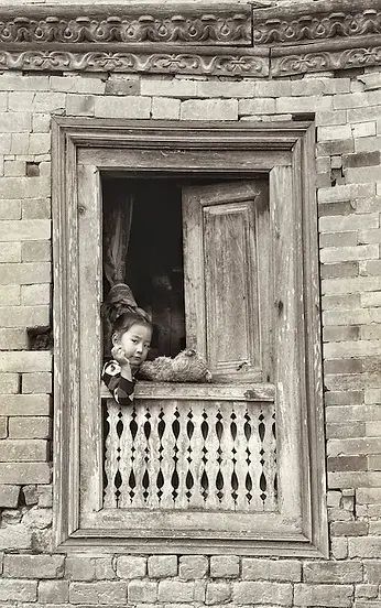 Bambina affacciata a una finestra di legno nei vicoli di Bhaktapur, tra sguardi curiosi e vita quotidiana da scoprire in viaggio con i bambini.