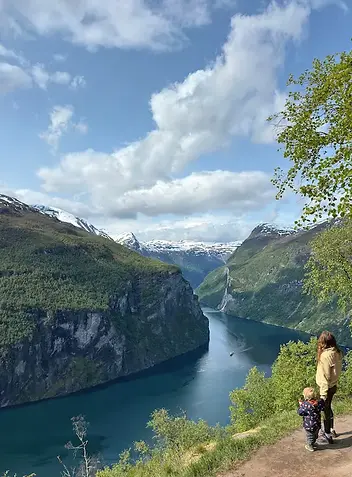 Mamma e bambino mano nella mano osservano il Geirangerfjord, tra montagne e riflessi d’acqua, in un’esperienza di viaggio condivisa.