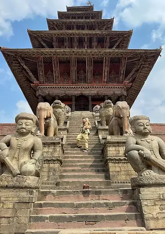 Papà e figlio sulla scalinata di un tempio a Bhaktapur, tra statue e mattoni antichi, durante un viaggio in famiglia alla scoperta del Nepal.