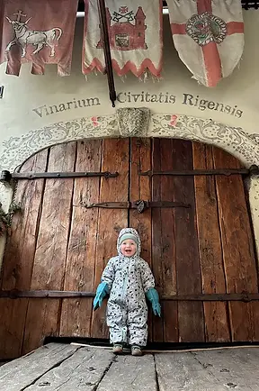 Bambino davanti all’ingresso di una locanda medievale a Riga, portone antico e drappi sullo sfondo