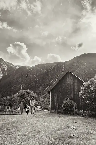 Mamma e figlio che passeggiano tra le antiche fattorie norvegesi, circondati da prati verdi e silenzio, in un momento di viaggio semplice e condiviso.