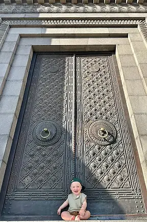 Bambino seduto davanti a un imponente portone monumentale nel centro di Erevan, con elementi architettonici tradizionali armeni.