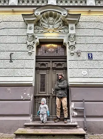 Papà e figlio davanti l'ingresso di edificio Art Nouveau a Riga con decorazioni floreali e linee curve.