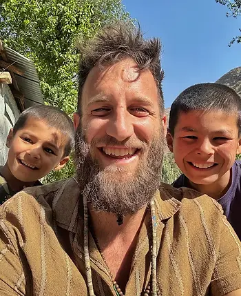 Mattia Melegari con due bambini sorridenti in Tajikistan, durante un momento di incontro e condivisione.