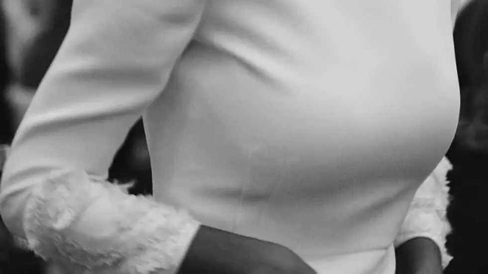 Novia con vestido blanco de manga larga con botones y encaje. Fondo desenfocado en blanco y negro. Ambiente elegante y formal.