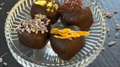 Selbstgemachte Schoko-Himbeer-Lovebites auf einer eleganten Glasplatte, dekoriert mit Lavendelblüten, gehackten Pistazien, getrockneter Ananas und feinen Chili-Fäden.