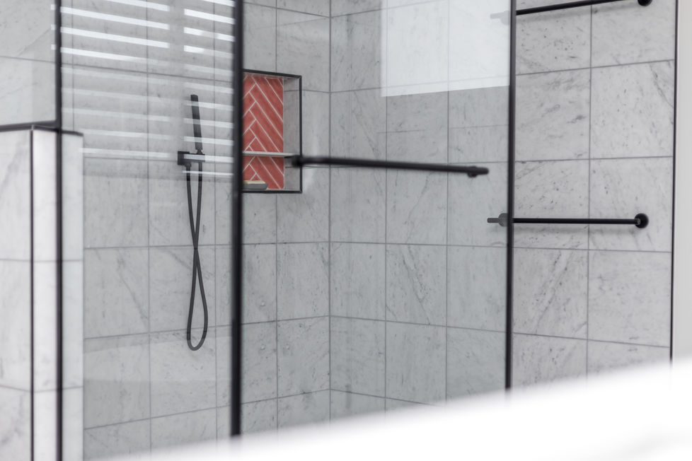 Modern bathroom remodel in Austin, TX featuring a marble-tiled walk-in shower with black-framed glass, matte black fixtures, and a bold coral herringbone tile niche for added design contrast.