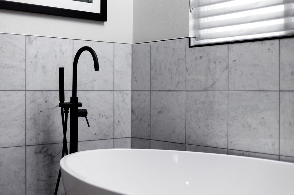 Close-up of a matte black freestanding tub filler against a polished marble tile wall in a luxury bathroom remodel in Austin’s University Hills.