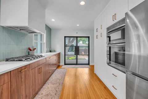 Sleek kitchen remodeling with walnut base cabinets, white upper cabinetry, and black-framed glass slider leading to a backyard patio in Austin, TX.