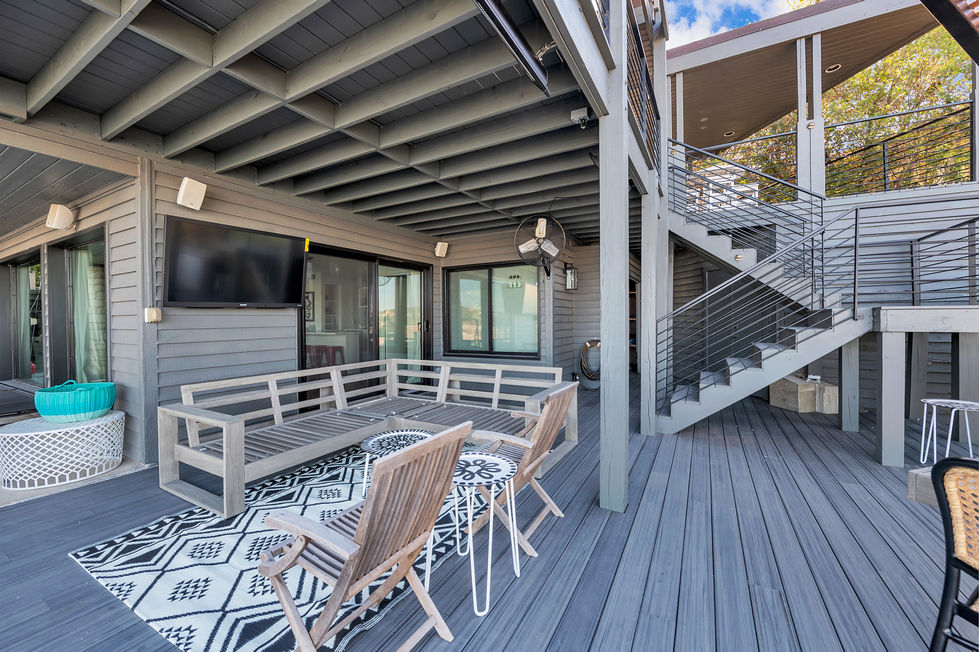 Stylish covered patio remodel with wood lounge seating, mounted outdoor TV, and geometric area rug for lakeside relaxation in Austin, TX.