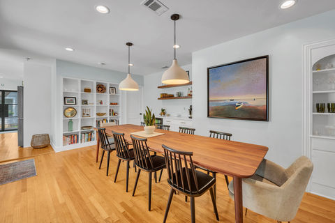 Dining room remodeling in Austin, TX featuring mid-century modern white cabinetry, bold wall art, pendant lighting, and a walnut dining table.