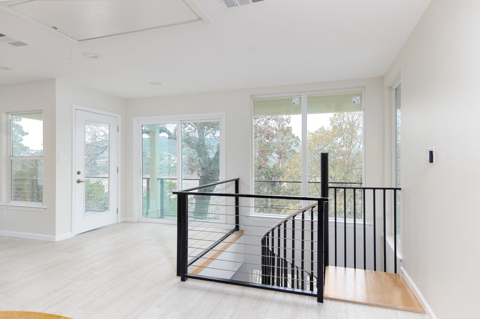 Interior remodeling in Austin, TX with transitional design, light-toned tile flooring, and expansive windows overlooking Lake Travis, connected by a sleek metal railing staircase.