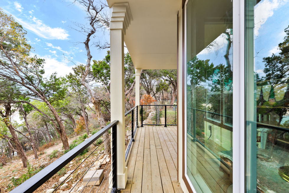 Remodeled balcony in Austin’s Lake Travis area with natural wood decking, modern railing, and serene hill country landscape views from a transitional-style home.