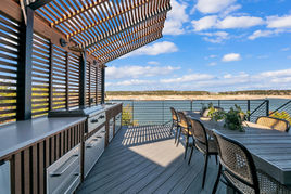 Remodeled Lakeway deck with open-air kitchen, featuring wood-slat pergola, high-end cabinetry, and dining area overlooking scenic waterfront.
