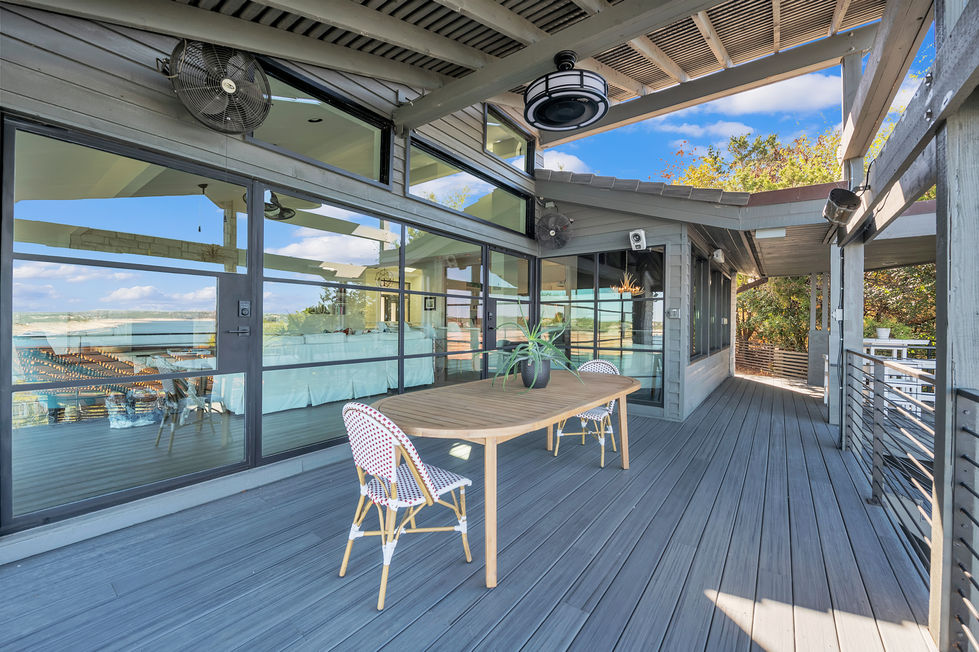 Outdoor living space remodel with bistro-style seating, wood decking, and expansive glass facade reflecting natural surroundings for seamless indoor-outdoor flow.