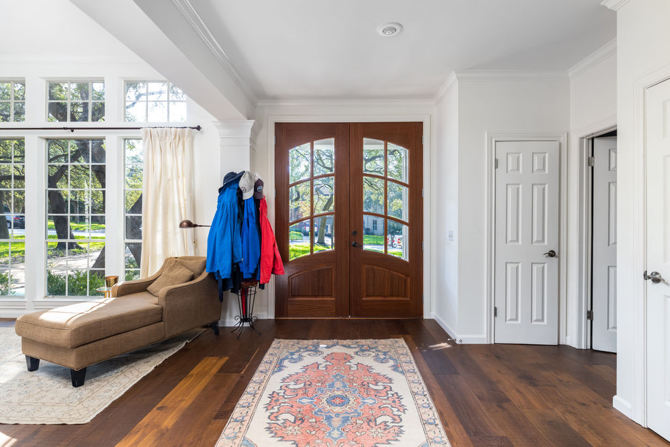 Remodeled foyer with warm transitional design, featuring rich hardwood floors, double wood front doors, and abundant natural light from grid-style windows in Austin, TX.