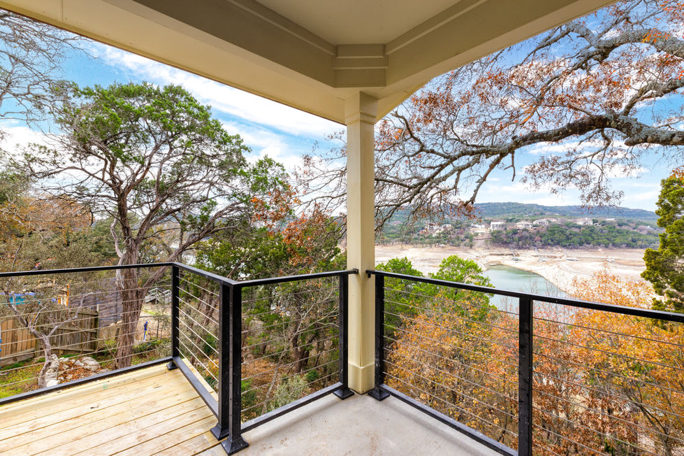 Covered balcony remodel with cable railing offering unobstructed views of Lake Travis and surrounding hillside homes, emphasizing outdoor living in Austin, TX.