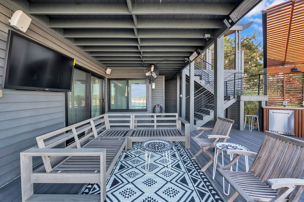 Covered lounge area renovation with outdoor TV, gray wood sectional, and tribal-pattern rug in a contemporary Austin, TX lakeside home.