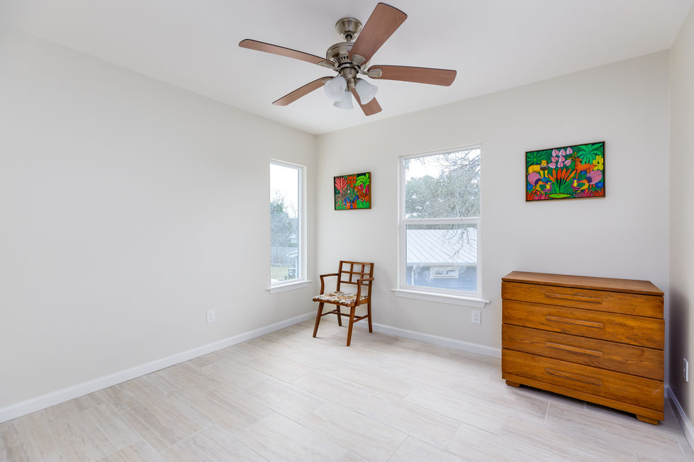 Remodeled guest bedroom with neutral ceramic tile floors, clean walls, and vibrant tropical artwork, embracing a minimalist transitional aesthetic in Austin, TX.