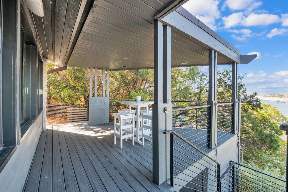 Outdoor deck remodel featuring modern composite flooring, minimalist white dining set, and cable railing surrounded by nature in Austin, TX.
