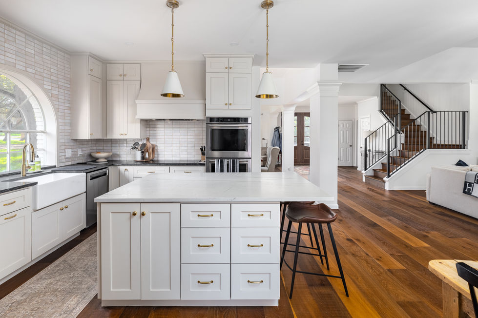 Remodeled kitchen with shaker-style white cabinets, marble island, warm wood flooring, and elegant gold pendant lighting in Austin, TX.