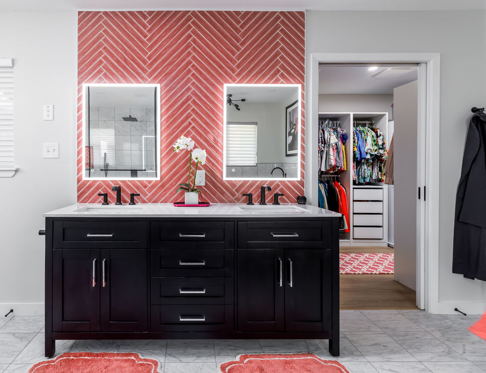 Contemporary bathroom remodel featuring a double vanity with black cabinets, vibrant coral herringbone tile backsplash, and LED-lit mirrors in a bold, modern interior design style in Austin’s University Hills neighborhood.