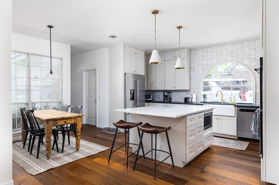 Kitchen remodel with farmhouse and transitional influences, featuring marble island, brass pendant lights, white cabinetry, and rustic wood dining table on wide-plank floors in Austin, TX.