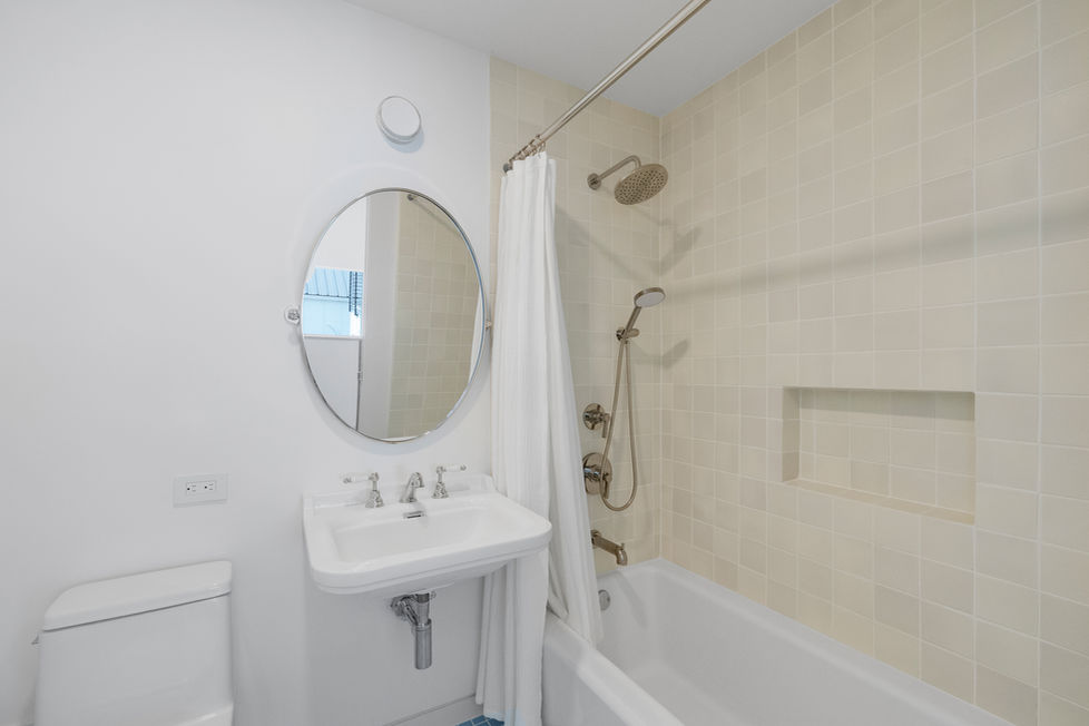 Guest bathroom in a new construction home with pedestal sink, tub shower, neutral tile walls, and clean modern detailing.