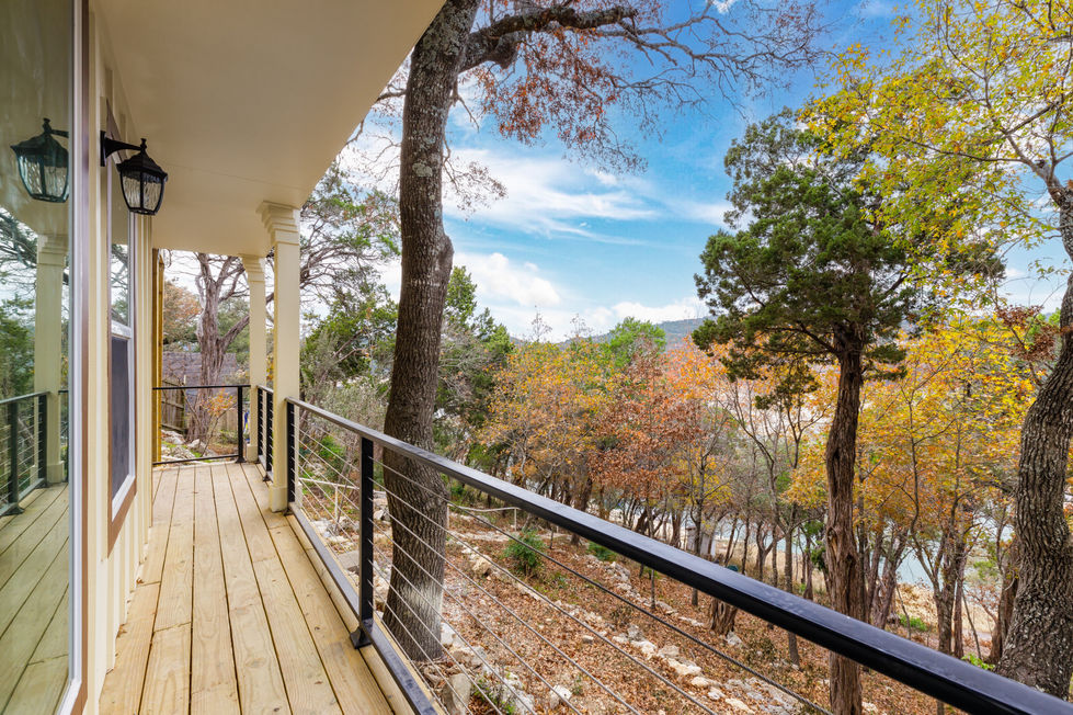 Outdoor remodeling project in Lake Travis showcasing a covered balcony with wood decking, horizontal cable railing, and panoramic views of Austin’s hill country landscape.